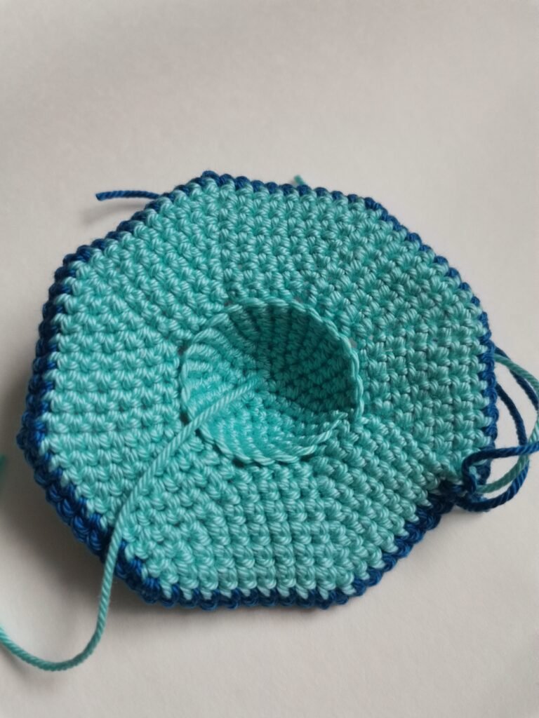 Crochet process of the bottom part of amigurumi flying saucer in light blue yarn.