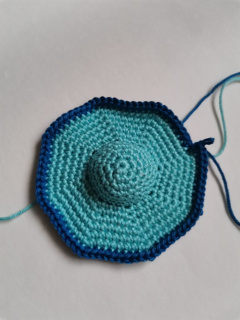 Crochet process of the bottom part of amigurumi flying saucer in light blue yarn.