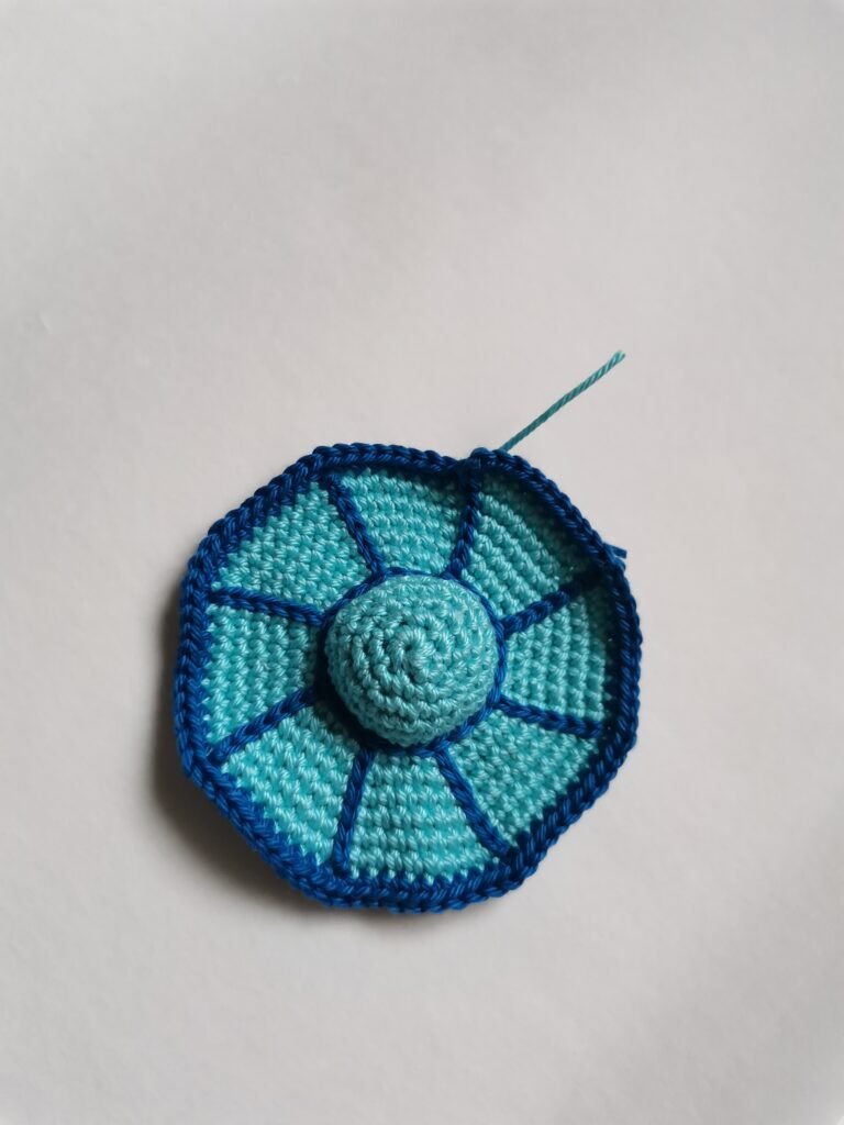 Crochet process of the bottom part of amigurumi flying saucer in light blue yarn.