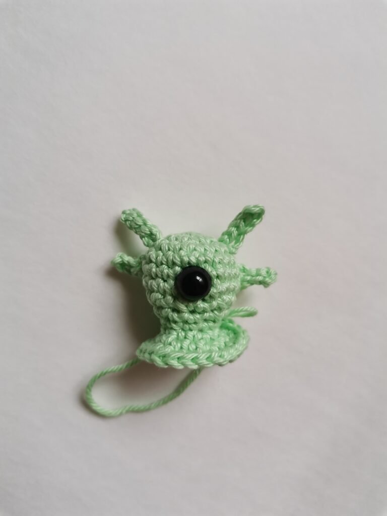 Close up of amigurumi alien head with safety eye and small horns.
