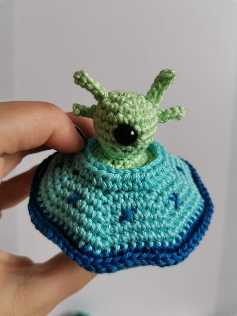Hand holding a finished crochet UFO flying saucer toy showing the size and detailed texture of the cotton yarn.
