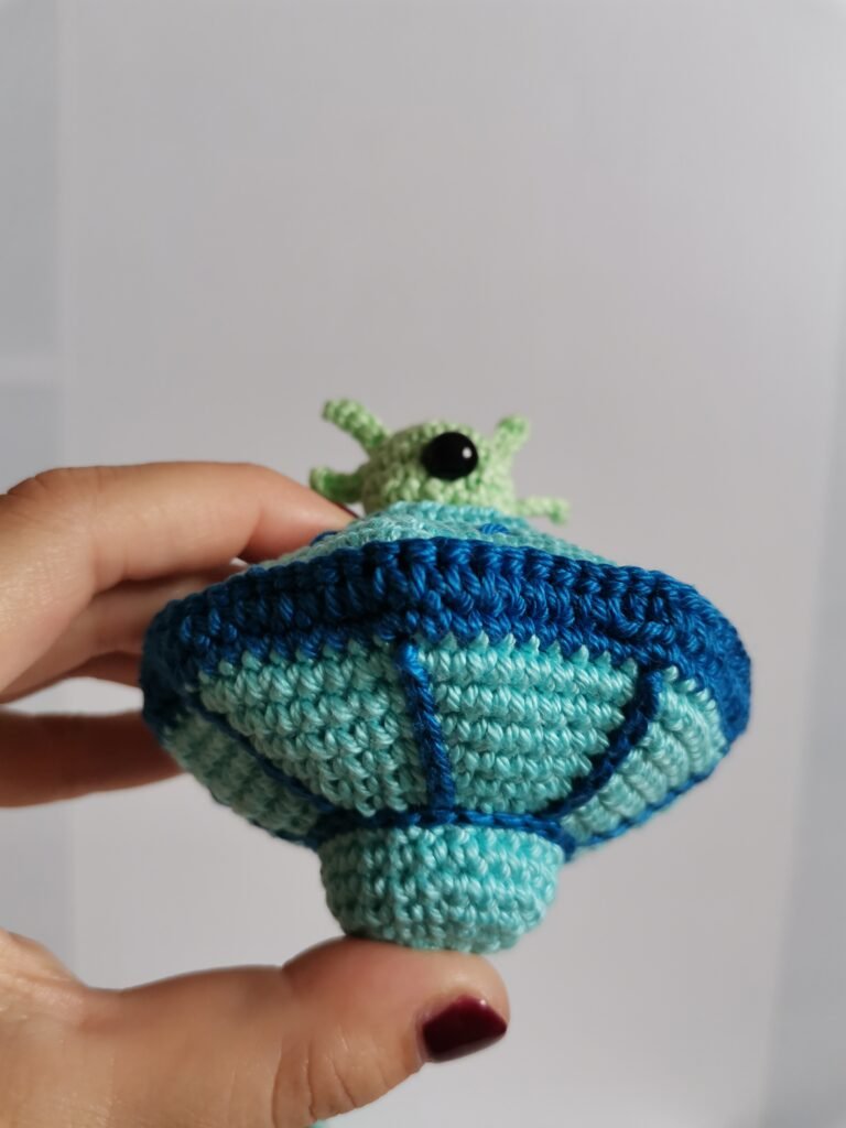 Hand holding a finished crochet UFO flying saucer toy showing the size and detailed texture of the cotton yarn.