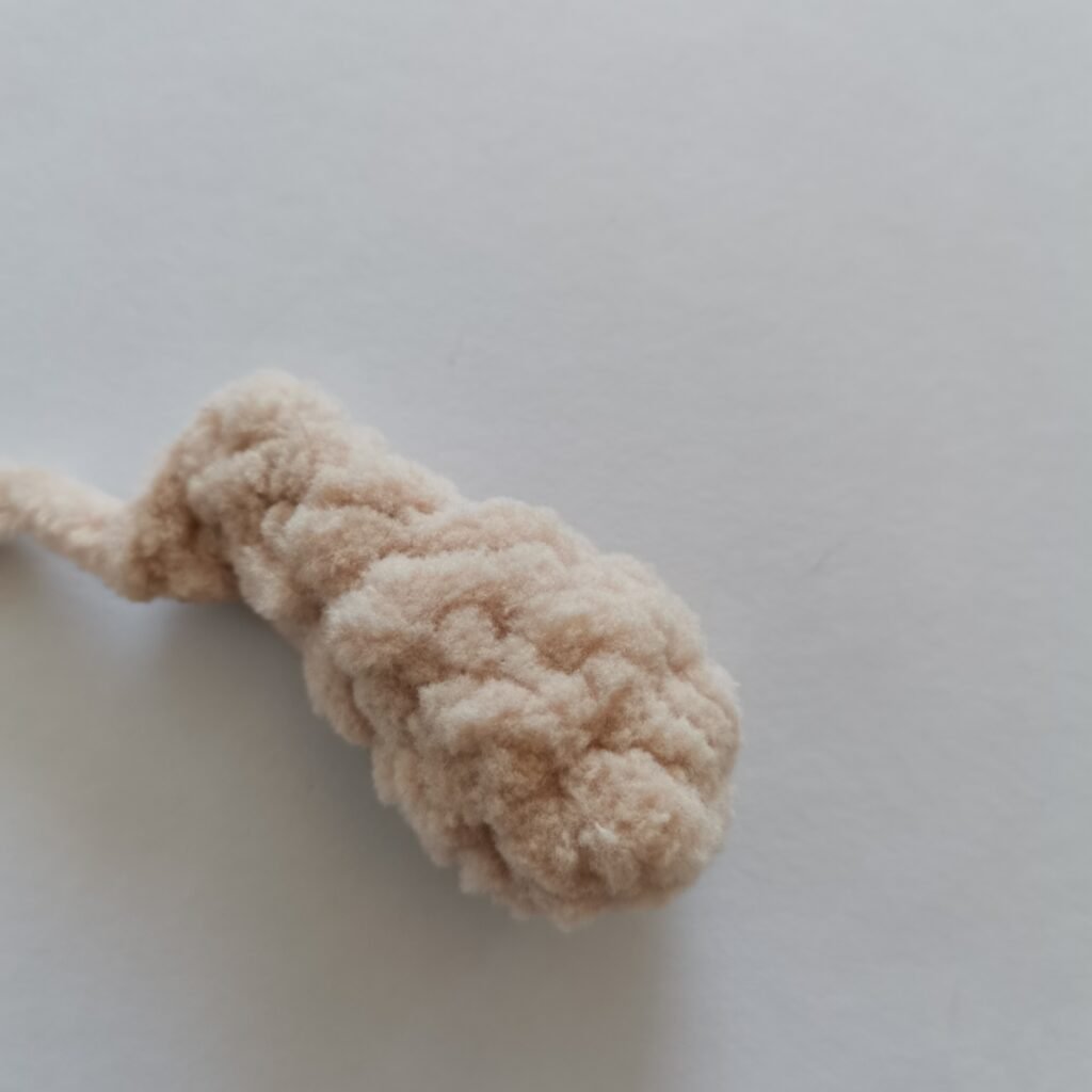 Close-up of a small, crem-colored crochet bunny arm made with soft plush yarn.