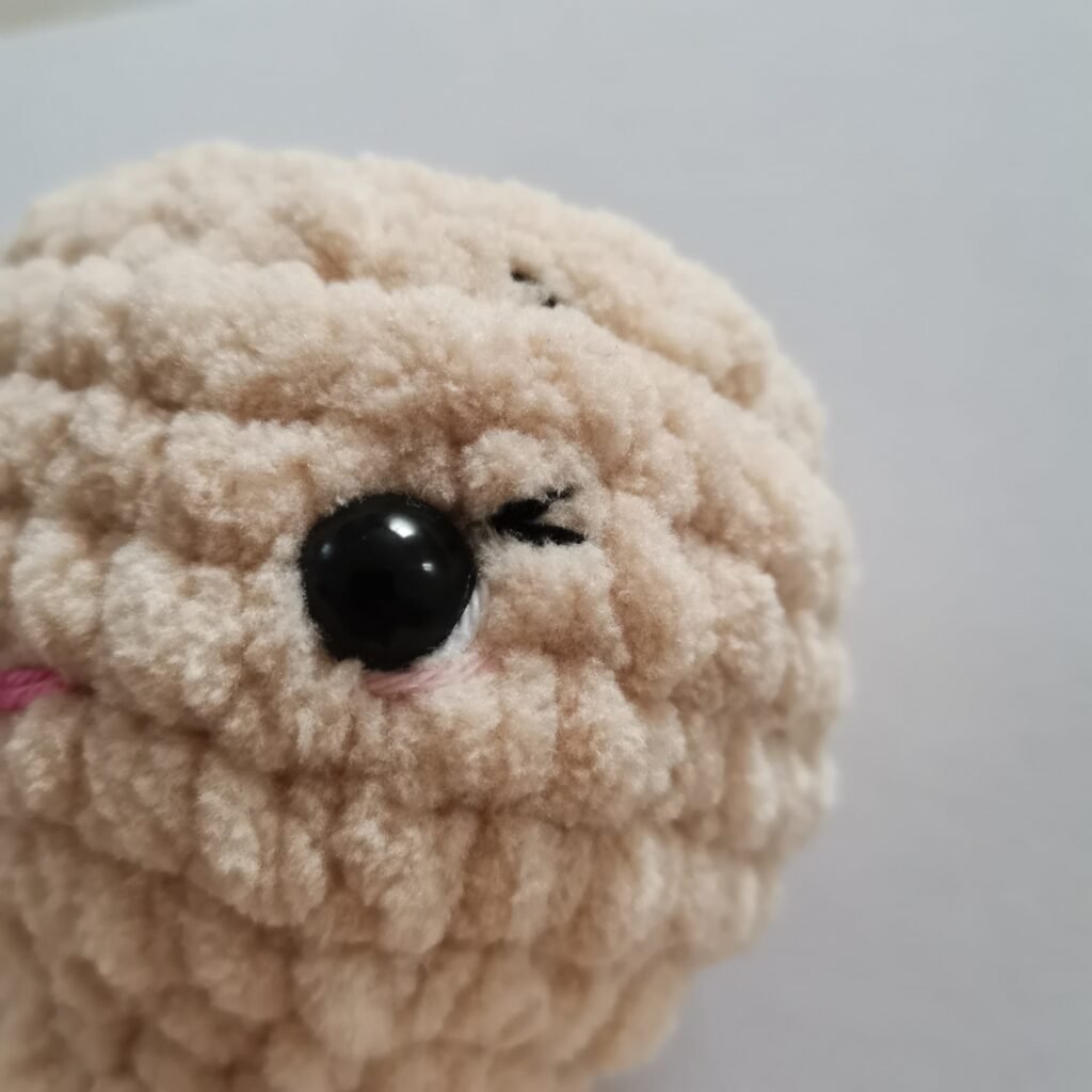 Close-up of a head and eyes of cream-colored crochet bunny made with soft plush yarn.