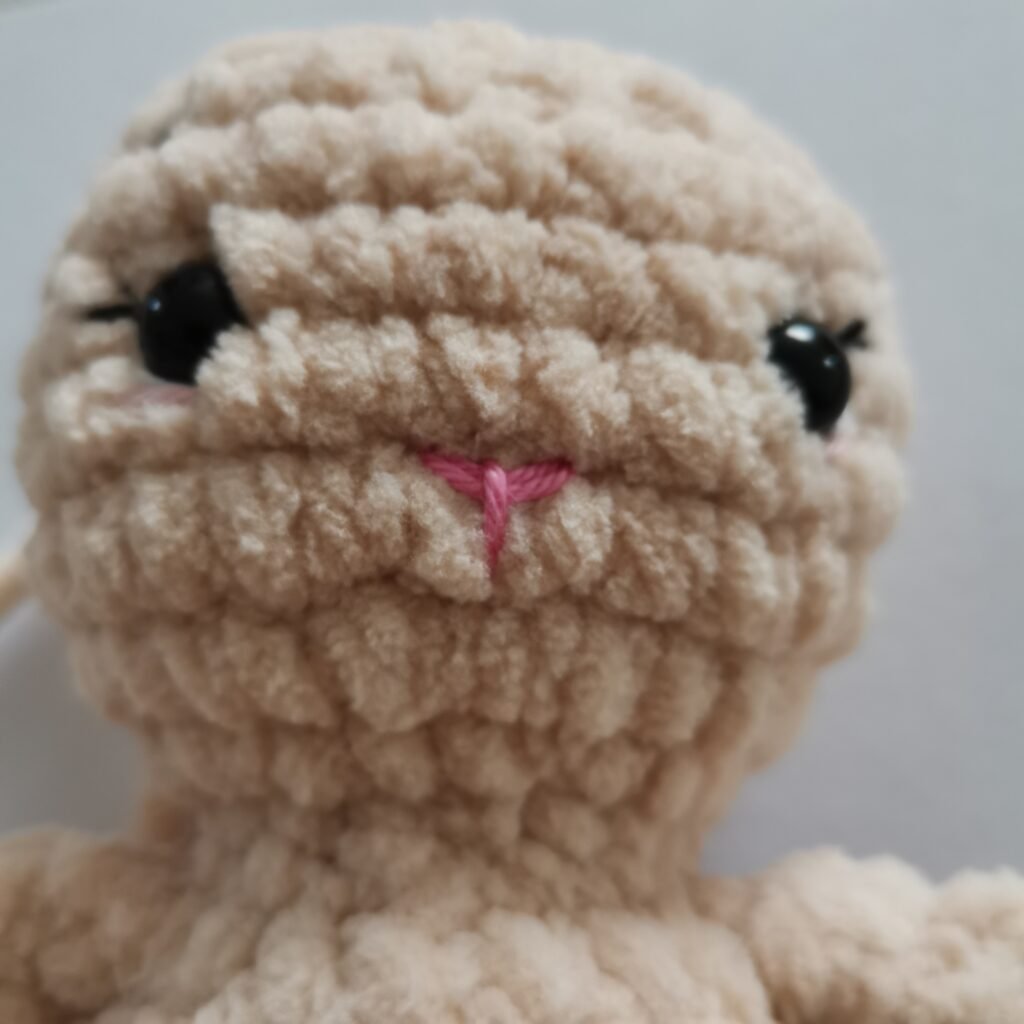 Close-up of a head and mouth of cream-colored crochet bunny made with soft plush yarn.