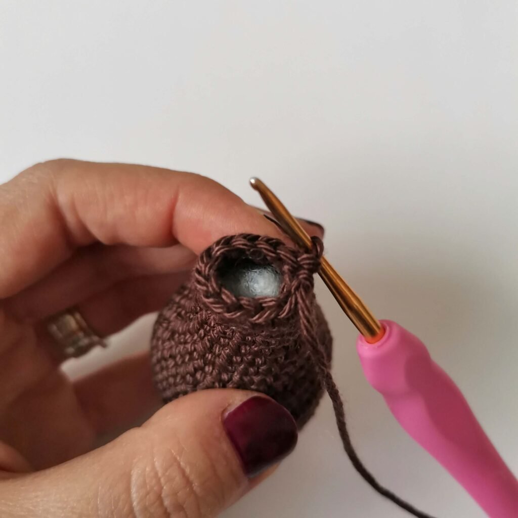 Close up of stuffing a crochet teddy bear leg with fiberfill while using a pink crochet hook - EmmaS Dolls amigurumi tutorial.
