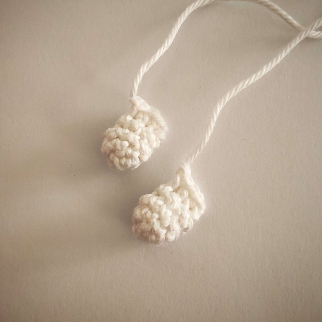 Two small white crocheted arms with long yarn tails for a free crochet ghost pattern.